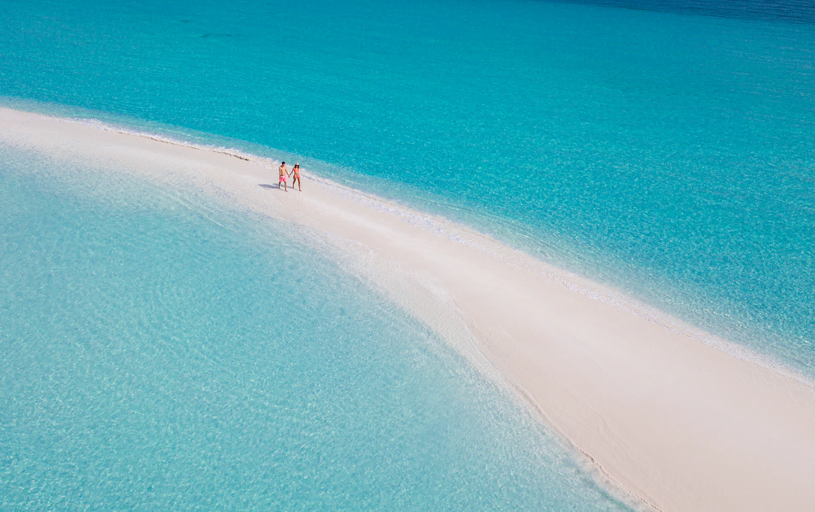 A couple walking a long white sandbank in a turquoise Maldives lagoon