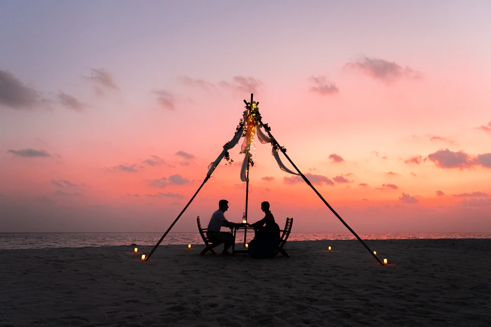 Wider sunset view of a couple at a private beach dinner setup