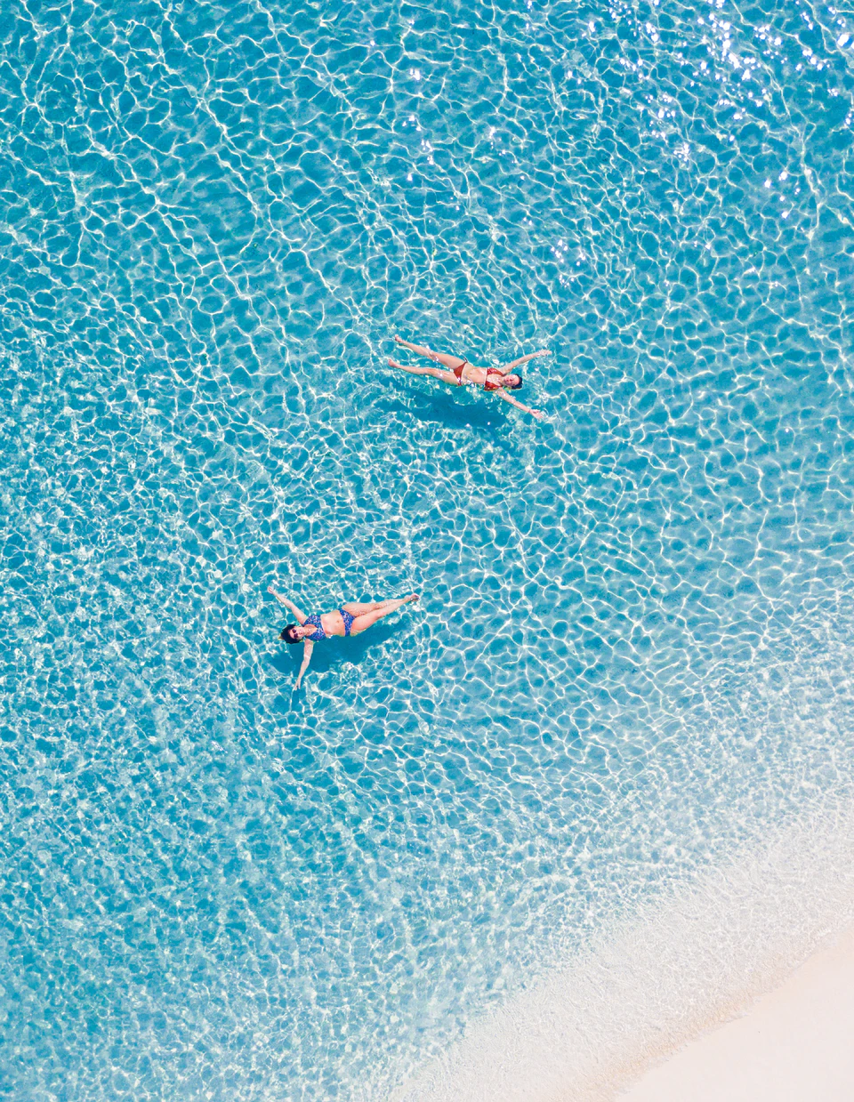 Top-down view of two swimmers in rippled turquoise water