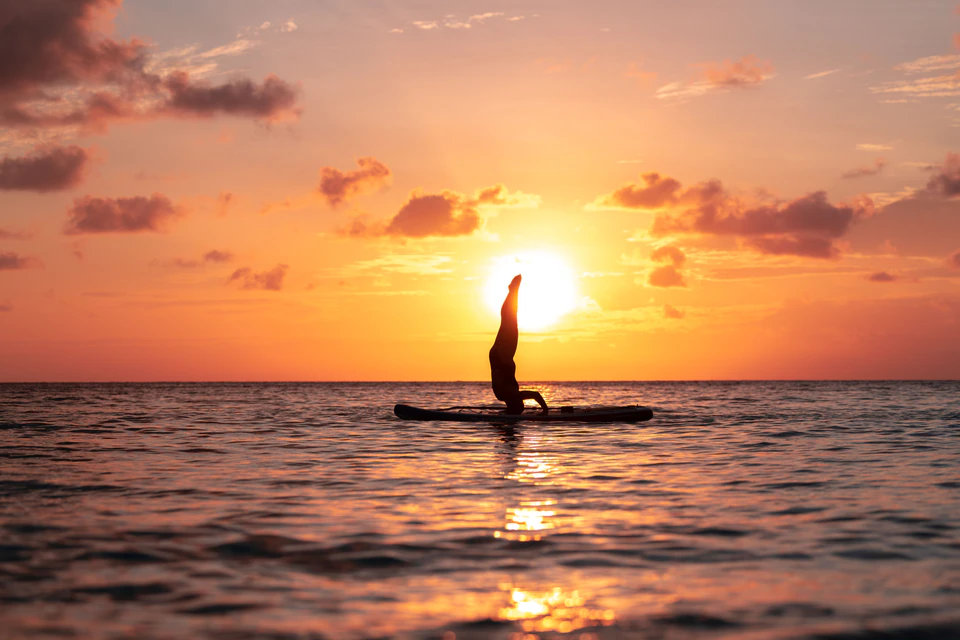 Solo stand-up paddleboarder silhouetted in the sunset reflection