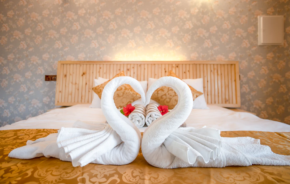 Wide close-up of towel swans and flower petals on the bed